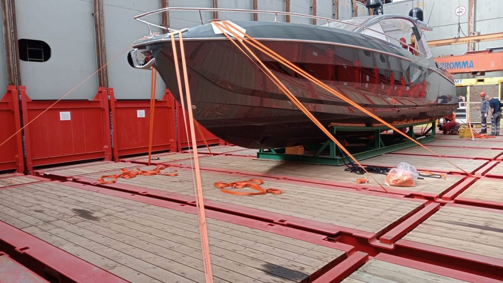 A luxury yacht secured with orange lashing straps on a flat rack container onboard.