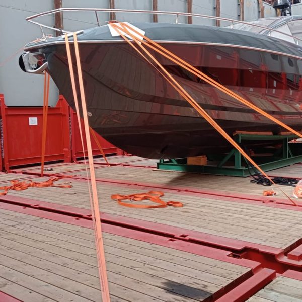A luxury yacht secured with orange lashing straps on a flat rack container onboard.
