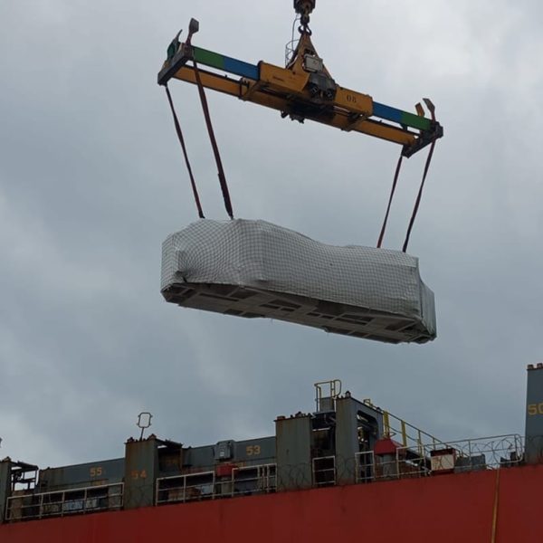Heavy machinery wrapped in protective white film being lifted onto a container ship.