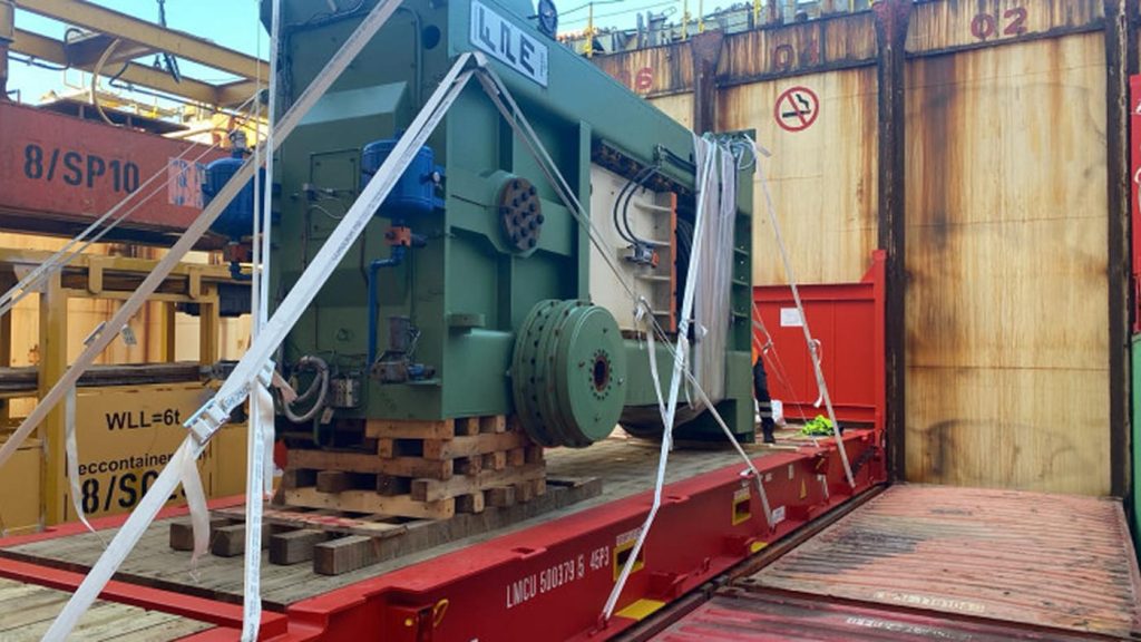 A large industrial press machine secured on a flat rack with heavy-duty straps.