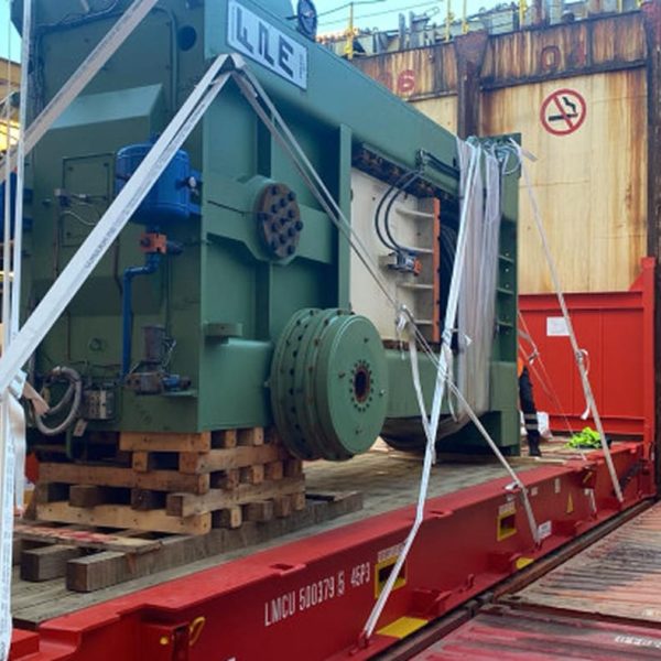 A large industrial press machine secured on a flat rack with heavy-duty straps.