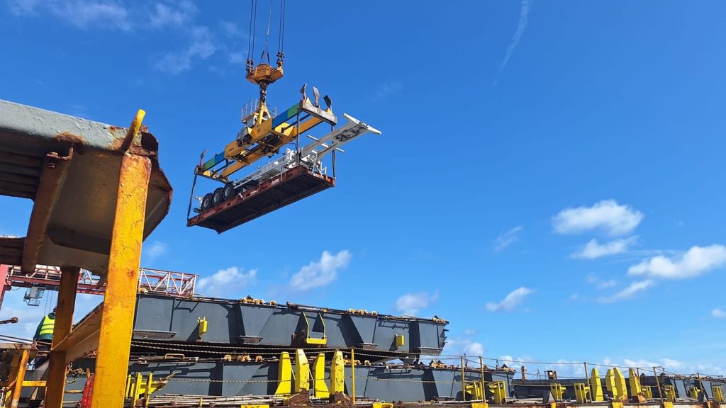 A port crane lifting a heavy-duty trailer onto a container ship.