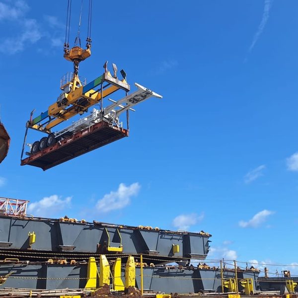 A port crane lifting a heavy-duty trailer onto a container ship.