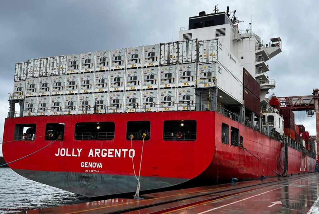 Rear view of the Jolly Argento docked at port, loaded with stacks of white reefer containers.