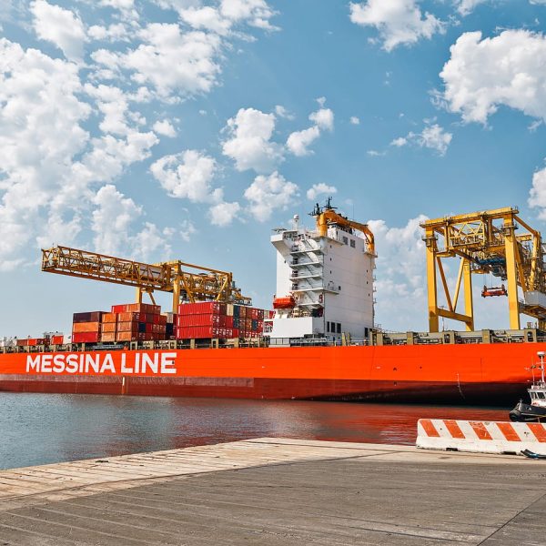 Side profile of the Jolly Giada container ship docked under large yellow port cranes.