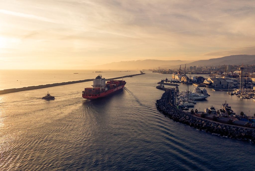 Aerial sunset view of the Jolly Oro container ship leaving the port accompanied by a tugboat.