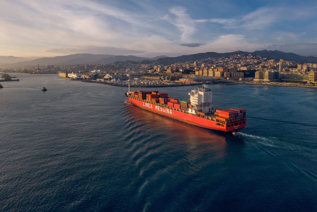 High-angle aerial shot of the Jolly Oro sailing near the coast during golden hour.