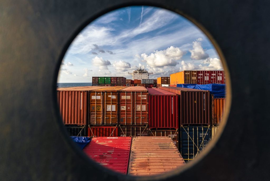 Creative view of the Jolly Verde deck and container stacks seen through a circular ship porthole.