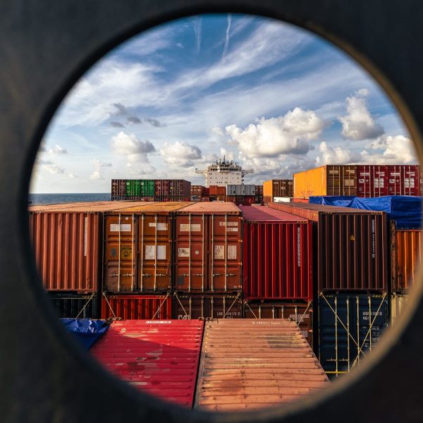 Creative view of the Jolly Verde deck and container stacks seen through a circular ship porthole.
