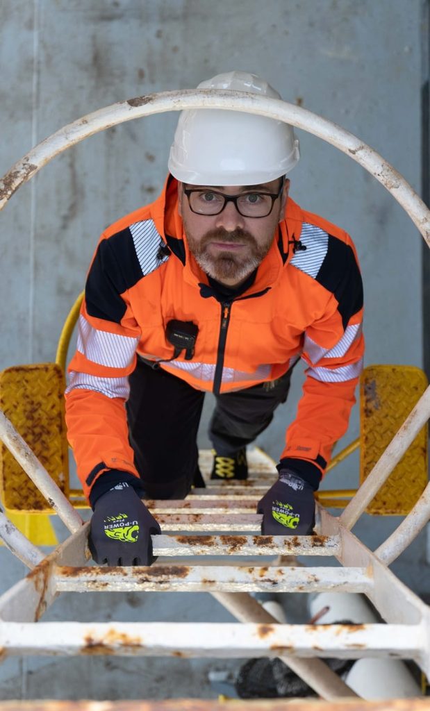 Crew member in high-visibility gear climbing a vertical ship ladder.