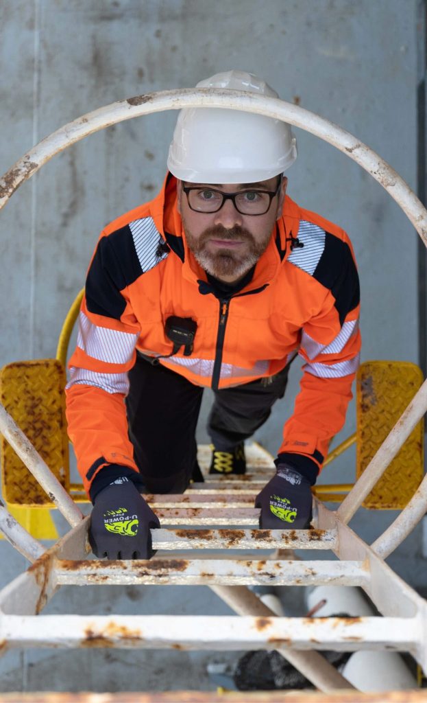 Membro dell'equipaggio in attrezzatura ad alta visibilità che sale su una scala verticale della nave.