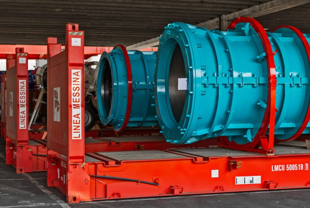 Large blue industrial cylinders secured on red Messina Line flatrack containers.