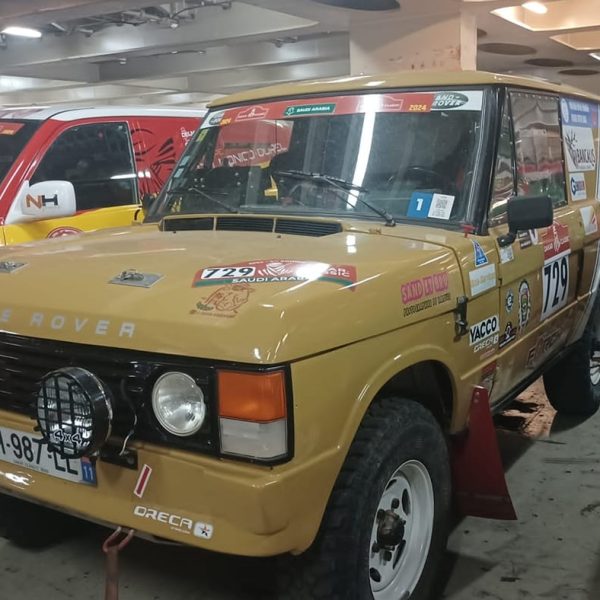 A classic tan Range Rover rally car parked inside the ship's hold among other Dakar vehicles.