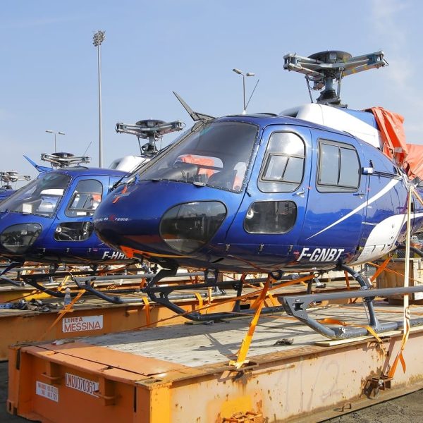 A row of blue helicopters secured on Linea Messina flatrack containers at the port.