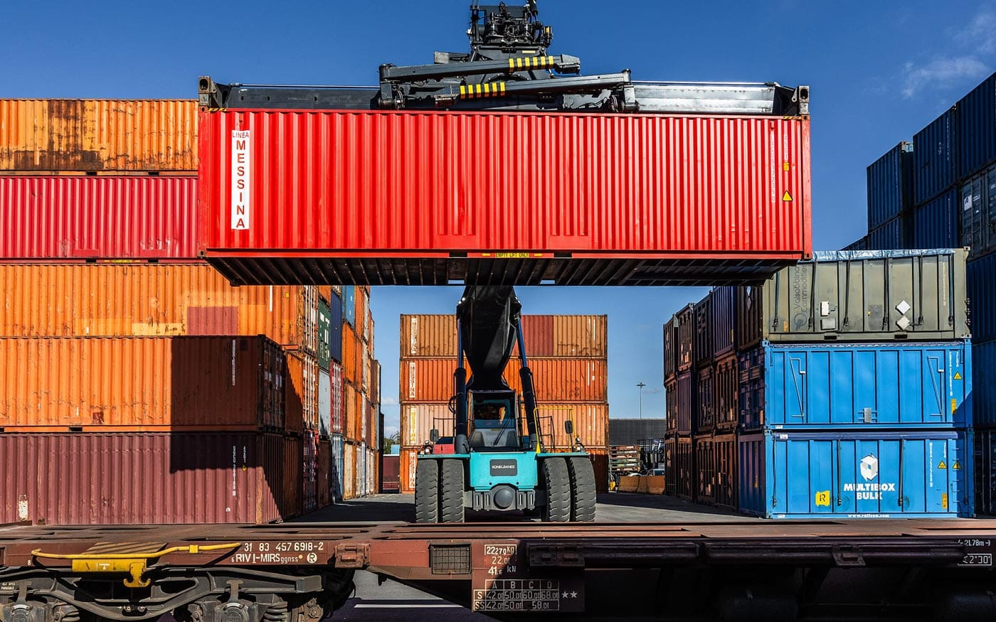 A reach stacker lifting a red Linea Messina container from a rail wagon during multimodal operations.